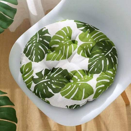 Round green leaf-patterned cushion on a white chair with a wooden floor.