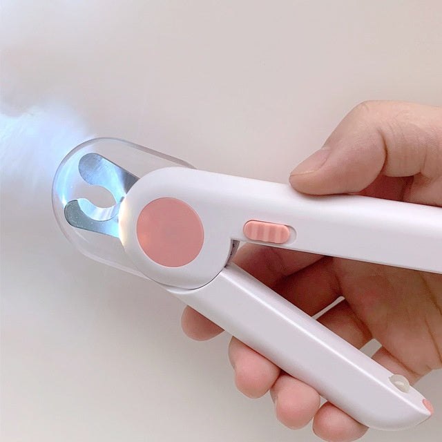 A hand holding a pair of LED pet nail clippers with a pink non-slip handle and built-in LED light being used on a pet's nail.